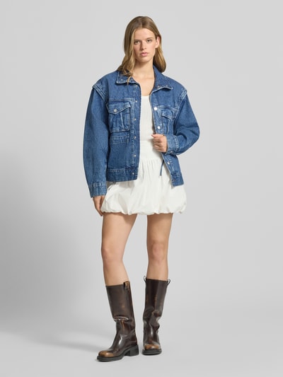 Frauenmodel trägt Jeansjacke mit Pattentaschen Modell 'Isabel' von Gina Tricot aus Reine Baumwolle, Straight Fit, Umlegekragen, Druckknopfverschluss, Ganzkörperansicht von vorne.