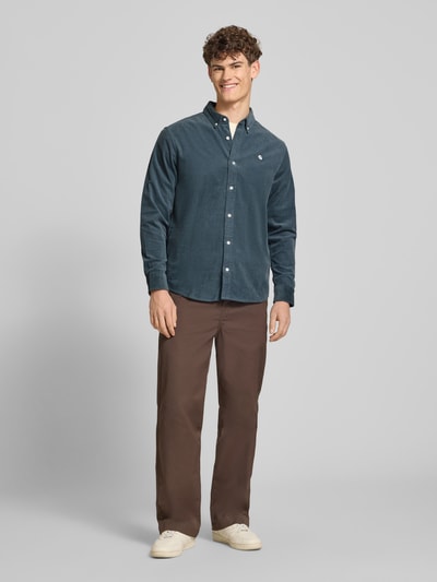 Męski model nosi Regular Fit Freizeithemd aus Cord mit Button-Down-Kragen od Carhartt Work In Progress, niebieski, bawełna, model 'Madison', krój regular fit, label-stitching, długość tyłu w rozmiarze M: 76 cm, szerokość w rozmiarze M: 44 cm, długość rękawa w rozmiarze M: 64 cm, widok całej sylwetki z przodu.