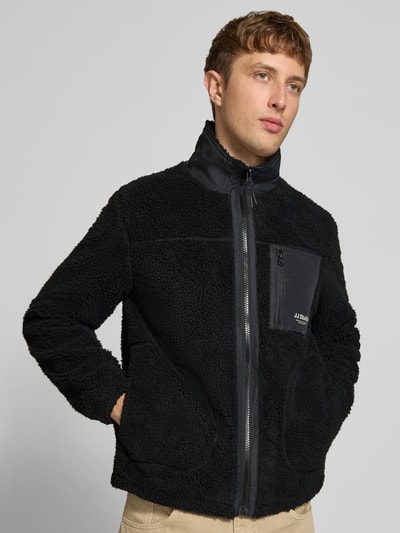 Männermodel trägt zwarte Fleecejacke met Teddybont, opstaande kraag, ritssluiting, Steekzakken, borstzak met rits, Logo, regular fit Model 'SOHO' van JACK & JONES, Ruglengte maat M 68 cm, Mouwlengte maat M 69 cm, Ganzkörperansicht von vorne