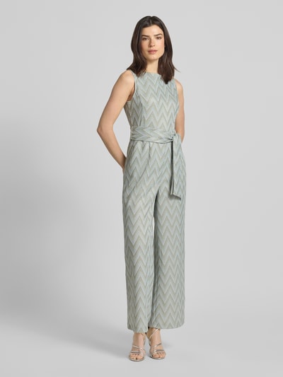 Frauenmodel trägt Regular Fit Jumpsuit mit geometrischem Allover-Stitching von Betty Barclay in sanften Beige- und Grautönen, Ganzkörperansicht von vorne. Taillierte Passform mit abnehmbarem Stoffband, Ärmelloses-Design, U-Boot-Ausschnitt, Rückenlänge bei Größe 36: 141 cm, Brustweite: 32 cm, Innenbeinlänge: 73 cm, Gesamtlänge: 141 cm.