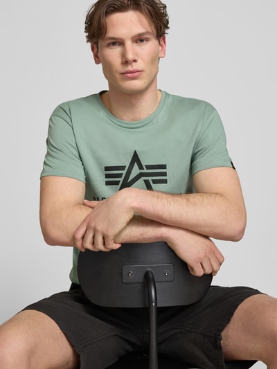 Männermodel trägt T-Shirt mit Logo und Rundhalsausschnitt von Alpha Industries in Mintgrün, reine Baumwolle, Regular Fit, Nahaufnahme Oberkörper.