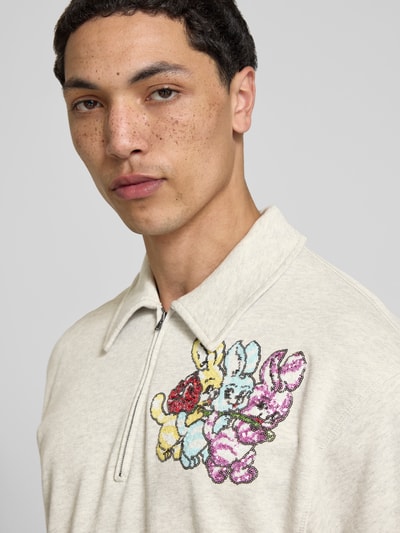Männermodel trägt Pullover mit Pailettenbesatz von Kenzo in Beige, Strick-Optik, reine Baumwolle, Troyer-Kragen, Nahaufnahme Oberkörper.