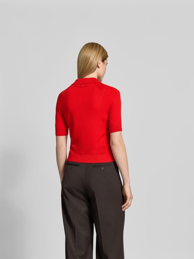 Frauenmodel trägt Poloshirt aus reiner Wolle von Victoria Beckham in Rot, Strick-Optik, Halbarm, Regular Fit, Ganzkörperansicht Rückansicht.