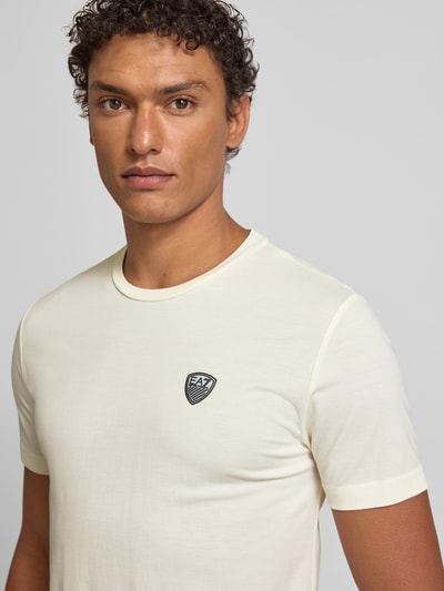 Męski model nosi T-shirt aus Viskose-Mix mit Label-Patch od EA7 Emporio Armani, okrągły dekolt, krój slim fit, jasny kolor, mieszanka wiskozy z dodatkiem streczu, naszywka z logo, długość tyłu 69 cm przy rozmiarze M, Nahaufnahme górnej części ciała.