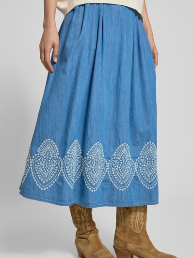 Frauenmodel trägt Midirock in Denim-Optik mit Stitchings von More & More aus Baumwoll-Lyocell-Mix, A-Linie, dekorative weiße Muster, Ganzkörperansicht von vorne.
