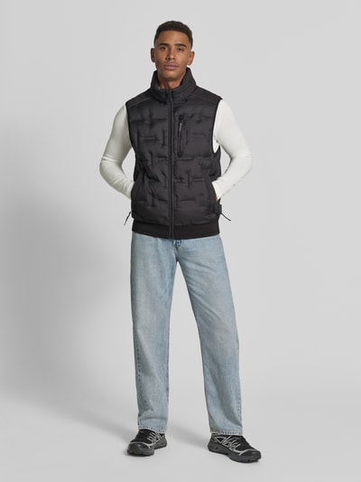 Männermodel trägt Regular Fit Outdoor-Weste mit reflektierenden Elementen von Tom Tailor, schwarz, glatte Textur, Ganzkörperansicht von vorne.