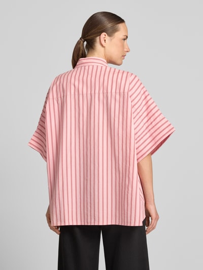 Frauenmodel trägt Oversized Kurzarmbluse aus reiner Baumwolle Modell 'JONKOE' von Essentiel Antwerp mit rosa und roten Streifen, Ganzkörperansicht Rückansicht.