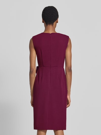 Frauenmodel trägt Knielanges Kleid mit Zierschleife von Adrianna Papell in Weinrot, taillierte Passform, Ganzkörperansicht Rückansicht. Elastischer Material-Mix, ärmellos, V-Ausschnitt, Wickel-Optik, Raffungen, Rückenlänge 95 cm, Brustweite 43 cm bei Größe 36.