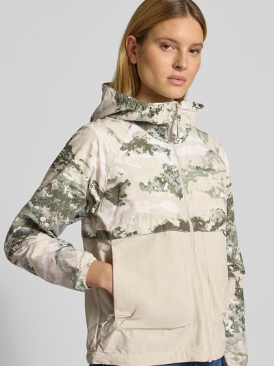 Modelka kobieca nosi kurtkę Regular Fit z kapturem model 'Spired Valley' od Columbia, nakładane kieszenie, beżowo-zielone odcienie z nadrukiem, długość tyłu w rozmiarze S: 59 cm, szerokość ramion w rozmiarze S: 42 cm, szerokość klatki piersiowej w rozmiarze S: 55 cm, długość rękawów w rozmiarze S: 60 cm, zdjęcie całej sylwetki z przodu