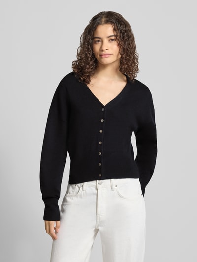 Modelka kobieca ma na sobie kardigan z mieszanki bawełny i wiskozy o kroju regular fit model 'Compact' marki Topshop, imitacja dzianiny, czarny, dekolt w serek, długość tyłu w rozmiarze S 50 cm, długość rękawa 55 cm, widok całej sylwetki z przodu.