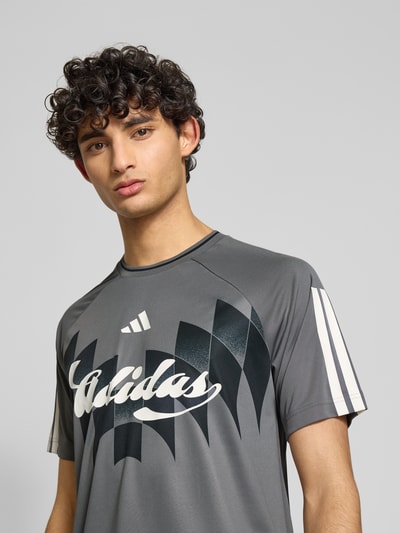 Männermodel trägt Regular Fit T-Shirt mit Label Print von adidas Sportswear, Optik: unifarben, Kontraststreifen, Kurzarm, Nahaufnahme Oberkörper.
