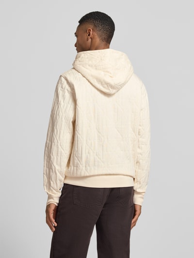 Männermodel trägt Hoodie mit Känguru-Tasche und Kapuze von Guess in Creme, Reine Baumwolle, Loose-Fit, elastische Abschlüsse, Rückenlänge 70 cm, Ärmellänge 68 cm, Ganzkörperansicht Rückansicht.