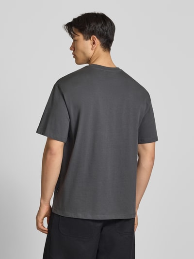 Männermodel trägt Oversized T-Shirt Modell 'FISHER' von Blend aus Reine Baumwolle in dunklem Grau, Rückenlänge 72 cm, Ganzkörperansicht Rückansicht.