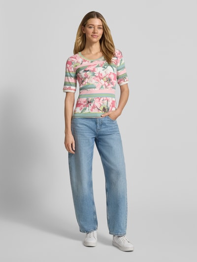 Modelka kobieca nosi T-Shirt mit floralem Allover-Print od Betty Barclay z elastycznej mieszanki bawełny, krój dopasowany, okrągły dekolt, półrękaw, całkowita długość 58 cm w rozmiarze 36, w pastelowych kolorach, wzór kwiatowy, widok całej sylwetki z przodu.