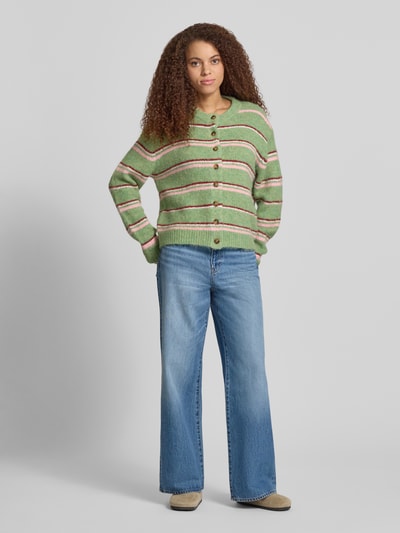 Frauenmodel trägt Cardigan mit Streifenmuster Modell 'CARO' von Topshop, Material-Mix mit Woll-Anteil, Relaxed-Fit, Rundhalsausschnitt, Knopfleiste, Streifen in Grün, Beige und Rosa, kombiniert mit Jeans, Ganzkörperansicht von vorne.