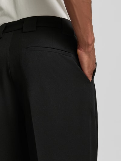 Mężczyzna nosi Stoffhose mit Bügelfalten und Eingrifftaschen od MCNEAL, czarny materiał, luźny krój, gładka tekstura, detal tylnej kieszeni, zbliżenie na biodra