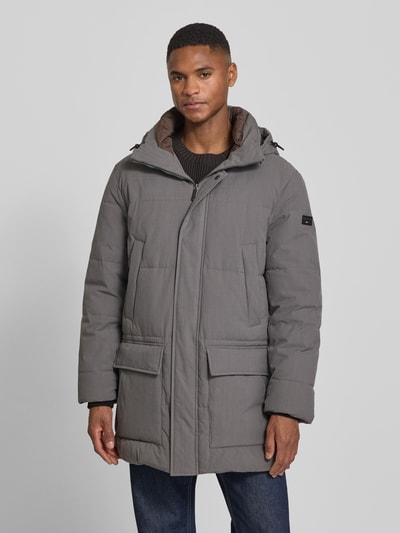 Męski model nosi Parka mit Kapuze od bugatti, krój regular fit, kaptur, stójka, wpuszczane i kieszenie z patką, długość tyłu w rozmiarze 52: 90 cm, szerokość ramion w rozmiarze 52: 48 cm, szerokość klatki piersiowej w rozmiarze 52: 61 cm, długość rękawów w rozmiarze 52: 70 cm, widok całej sylwetki z przodu.
