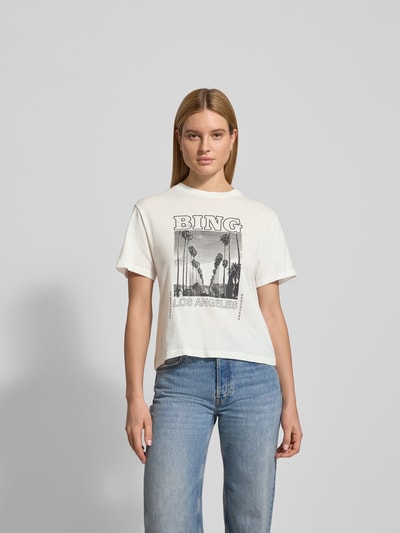 Frauenmodel trägt T-Shirt mit Statement-Print von Anine Bing, Reine Baumwolle, taillierte Passform, Rundhalsausschnitt, Motiv-Print, Ganzkörperansicht von vorne.