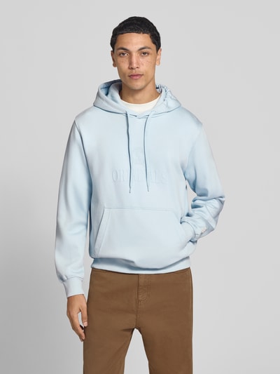 Männermodel trägt Hoodie aus Baumwoll-Mix Modell 'FREDERIKS' von JACK & JONES in Hellblau mit Kängurutasche, Ganzkörperansicht von vorne.