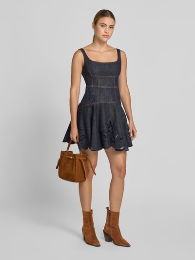 Frauenmodel trägt Bucket Bag in Suede-Optik von Tory Burch mit Logo-Detail, Magnetverschluss, Hauptfach, abnehmbaren Schulterriemen, Breite 23 cm, Länge 22 cm, Tiefe 10 cm, warmes Braun, strukturierte Oberfläche, Ganzkörperansicht von vorne.