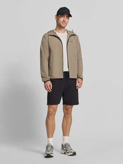 Männermodel trägt Regular Fit Trainingsjacke mit Label-Print Modell 'OW_Airynix JT HD 2' von BOSS Green in Beige, Ganzkörperansicht von vorne.