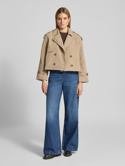 Männermodel trägt Boxy Fit Trenchcoat mit doppelreihiger Knopfleiste Modell 'CHLOE' von Vero Moda, unifarben, Umlegekragen, gun flap, kellerfalte, długi rękaw z regulowanym paskiem, boczne kieszenie, Ganzkörperansicht von vorne.