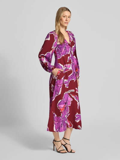 Frauenmodel trägt Midikleid aus Viskose-Mix mit V-Ausschnitt und Eingrifftaschen von Rich & Royal, florales Muster in Rot und Rosa, taillierter Schnitt, lange Ärmel, Ganzkörperansicht von vorne. Kleid mit Leinen-Anteil, Raffungen, seitlichen Taschen, rückseitigem Haken- und Reißverschluss, Rückenlänge 124 cm, Brustweite 40 cm, Ärmellänge 60 cm.