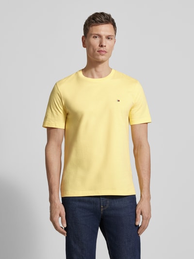 Mannenmodel draagt Regular Fit T-Shirt aus reiner Baumwolle van Tommy Hilfiger in effen geel, korte mouwen, logo-stiksel, ronde hals, jersey katoenmateriaal, regular fit, voorkant volledig zichtbaar, volledige lichaamsopname.