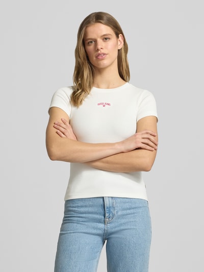 Vrouwenmodel draagt T-shirt in riblook met logo van Guess Jeans, mix van katoen en elastaan, slim fit, ronde hals, ruglengte maat S 54 cm, voorkant bovenlichaam close-up.