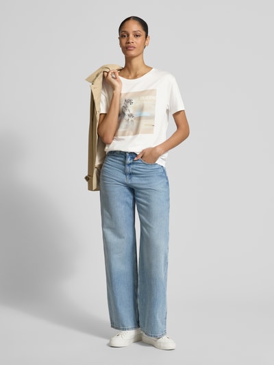 Frauenmodel trägt Regular Fit T-Shirt mit Strasssteinbesatz von monari, Reine Baumwolle, Motiv-Print, Kurzärmelig, Rundhalsausschnitt, Rückenlänge 55 cm, Ganzkörperansicht von vorne.