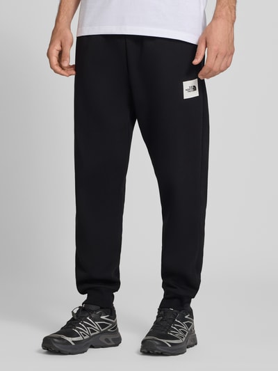 Mężczyznamodel nosi Regular Fit Sweatpants aus Escorial-Mix von The North Face, czarne, wpuszczane kieszenie, nadruk z logo, mieszanka wełny escorial i bawełny, krój regular fit, elastyczny pas z tunelem, długość wewnętrzna nogawki w rozmiarze M: 75 cm, całkowity widok z przodu.