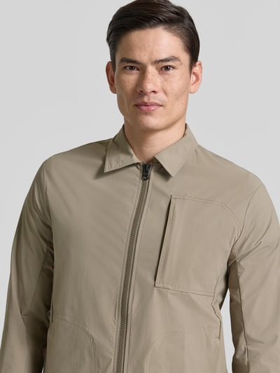 Männermodel trägt Regular Fit Jacke mit Umlegekragen Modell 'Motion' von SCANDINAVIAN EDITION aus Elastischer-Material-Mix in Beige, Nahaufnahme Oberkörper, Napoleontasche, Zweiwege-Reißverschluss, Eingrifftaschen, Rückenlänge bei Größe M 73 cm, Schulterbreite 45 cm, Brustweite 50 cm, Ärmellänge 66 cm.