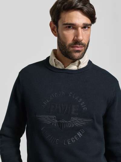 Męski model nosi Strickpullover aus reiner Baumwolle mit Logo-Stickerei von PME Legend, krój regular fit, okrągły dekolt, długi rękaw, prążkowane wykończenia, haftowane logo, kolor granatowy, półzbliżenie przód.