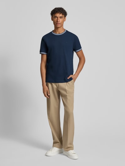 Männermodel trägt T-Shirt mit Kontraststreifen Modell 'Jose' von JOOP! Collection aus Baumwoll-Elasthan-Mix, Regular-Fit, navyfarben, Rundhalsausschnitt, beige Hose, weiße Schuhe, Ganzkörperansicht von vorne.