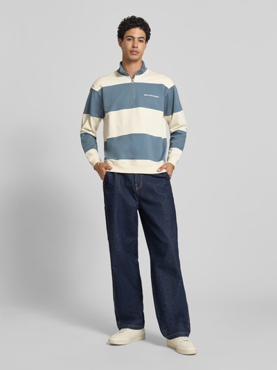 Męski model nosi Relaxed Fit Troyer aus reiner Baumwolle von Marc O'Polo Denim, niebiesko-kremowe szerokie paski, swetrowa faktura, długi rękaw, krótki zamek, widok całej sylwetki z przodu.
