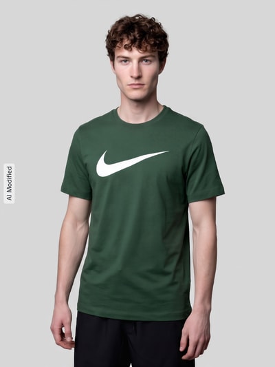 Männermodel trägt Regular Fit T-Shirt aus reiner Baumwolle von Nike in Dunkelgrün mit weißem Logo auf glattem Stoff, Nahaufnahme Oberkörper, KI-modifiziertes Bild.