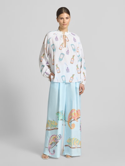 Frauenmodel trägt Wide Fit Seidenhose mit Motiv-Print von HERZENS, Reine Seide in Hellblau mit bunten Motiven, Elastischer Bund, Eingrifftaschen, Ganzkörperansicht von vorne.