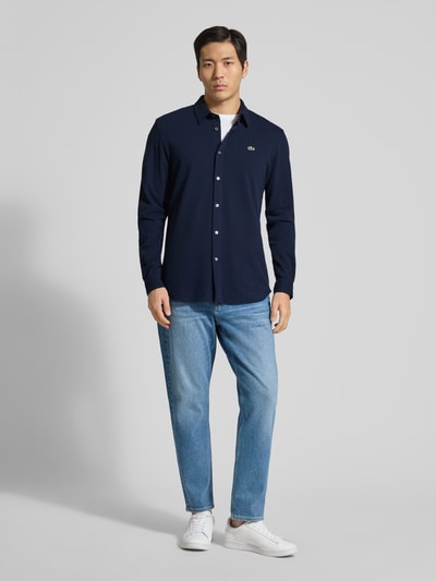 Männermodel trägt Slim Fit Freizeithemd aus reiner Baumwolle von Lacoste in Optik: Unifarben mit Kentkragen, Logo-Stitching, Piqué-Textur, Ganzkörperansicht von vorne.