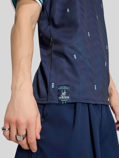 Männermodel trägt DFB Heimtrikot Deutschland 2026 von adidas in Mehrfarbig, Slim-Fit, Logo-Applikation, V-Ausschnitt, Kurzarm, Nahaufnahme Oberkörper.