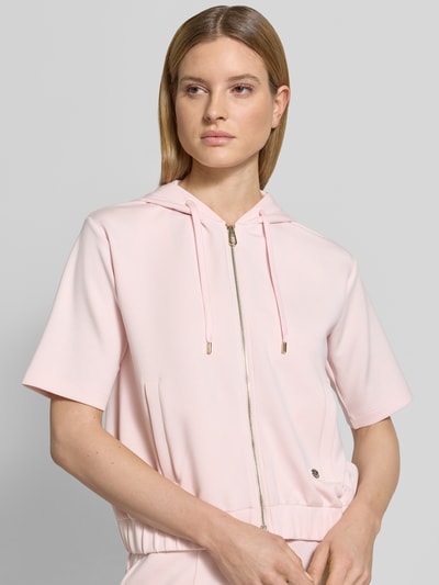 Frauenmodel trägt Sweatjacke mit Halbarm Modell 'Therese' von JOOP!, Elastischer-Material-Mix, Gerader-Schnitt, Kapuze, Reißverschluss, Halbarm, Label-Detail, Elastischer-Bund, Eingrifftaschen, zartrosa Farbton, glatte Textur, Nahaufnahme Oberkörper.