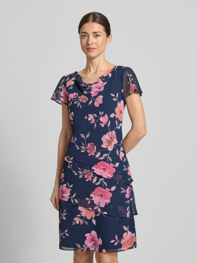 Frauenmodel trägt Knielanges Cocktailkleid mit Wasserfall-Ausschnitt von Christian Berg Cocktail, Chiffon, Taillierter Schnitt, Knielänge, Schmetterlingsärmel, Rock mit Drapierungen, Rückenlänge bei Größe 36: 97 cm, Brustweite bei Größe 36: 46 cm, Ärmellänge bei Größe 36: 16 cm, florales Muster, Ganzkörperansicht von vorne.