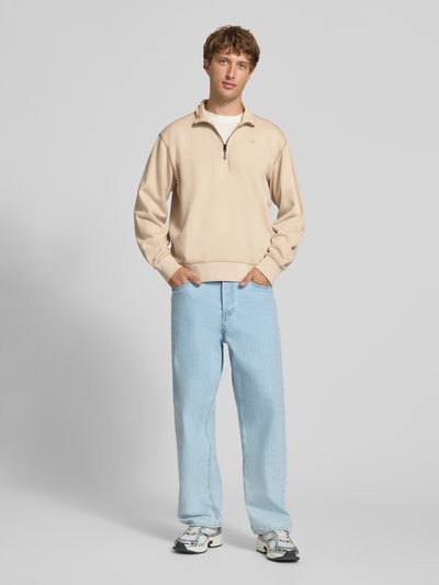 Männermodel trägt Regular Fit Sweatshirt aus reiner Baumwolle von G-Star RAW in Beige, kombiniert mit hellblauer Jeans, Ganzkörperansicht von vorne.