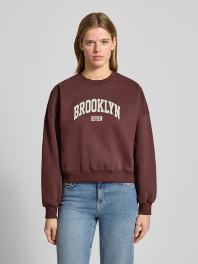 Frauenmodel trägt Sweatshirt mit Label-Print und Rundhalsausschnitt von Review aus Baumwoll-Mix, Relaxed-Fit, Ganzkörperansicht von vorne.