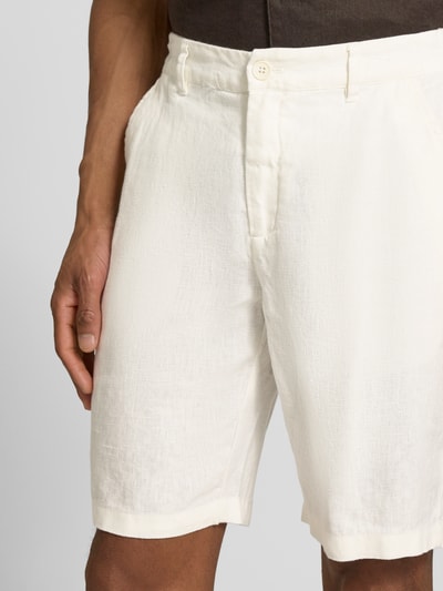 Mężczyzna nosi Leinen Shorts mit Eingrifftaschen Modell 'PANDRUP' od Casual Friday, białe, czysta len, krój straight fit, knop i zamek, tekstura widoczna, kieszenie boczne, szerokość w rozmiarze M: 44 cm, długość nogawki wewnętrznej: 23 cm, zbliżenie na górną część nóg z przodu.