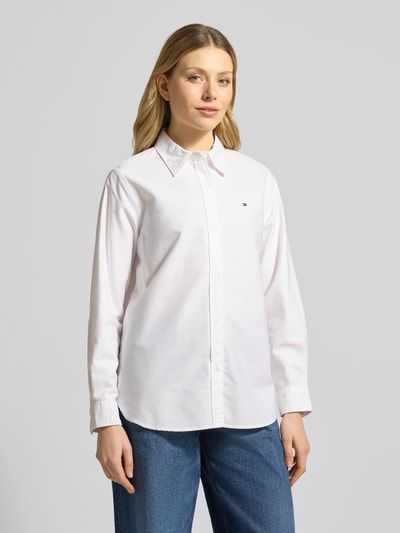 Vrouwenmodel draagt Relaxed Fit Hemdbluse aus reiner Baumwolle van Tommy Hilfiger, effen wit, oxford, logodetail, afgeronde rompzoom, overhemkraag, achterpas, manchet, eenrijige knoopsluiting, puur katoen. Ganzkörperansicht van voren.