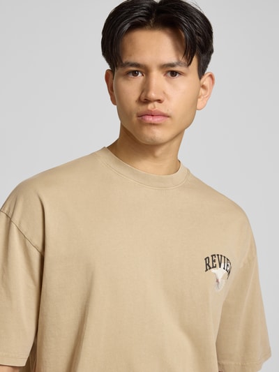 Männermodel trägt T-Shirt mit Logo- und Motiv-Print von REVIEW aus Reine Baumwolle, Loose-Fit, gerippter Rundhalsausschnitt, Nahaufnahme Oberkörper.