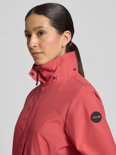 Frauenmodel trägt Parka mit Kapuze und verdecktem Reißverschluss von G.I.G.A. DX in Rot, glatte Oberfläche, Label-Patch am Ärmel, Nahaufnahme Oberkörper. Wassersäule 10.000mm, seitliche Reißverschlusstaschen, Gerader Schnitt.