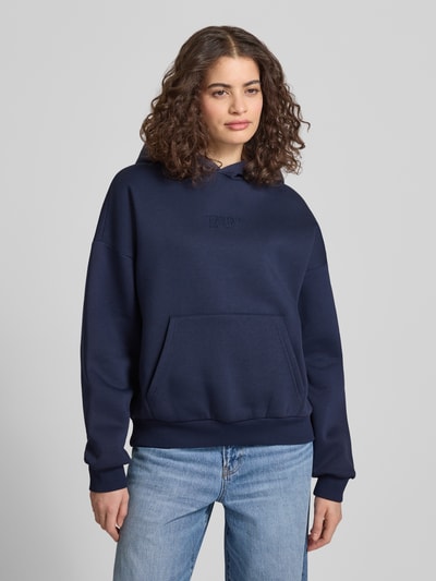 Modelka nosi Relaxed Fit Sweatshirt mit Logo-Print od Review, ciemnoniebieski, bawełniany, kieszeń kangurka, elastyczne wykończenia, krój relaxed fit, widok całej sylwetki z przodu.