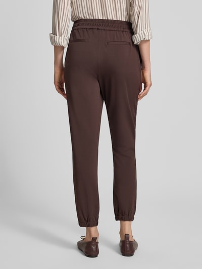 Frauenmodel trägt Jogger Pants mit Reißverschlusstasche Modell 'Jill' von monari in Braun, Straight Fit, elastischer Bund, Ganzkörperansicht Rückansicht.