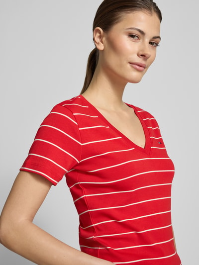 Vrouwenmodel draagt 'Slim Fit T-shirt uit zuiver katoen' van Tommy Hilfiger in tweekleurige look, gestreept motief, rode jersey, logodetail, V-hals, korte mouw, detailopname bovenlichaam.